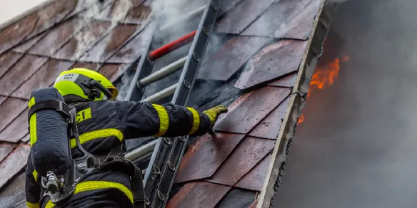 Bombeiro escalando telhado em chamas com uniforme antichamas, projetado para resistir ao calor extremo durante operações de resgate
