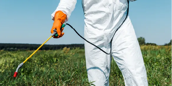 Pessoa aplicando inseticida em área rural, usando macacão com tecido antimosquito para proteção contra picadas de insetos
